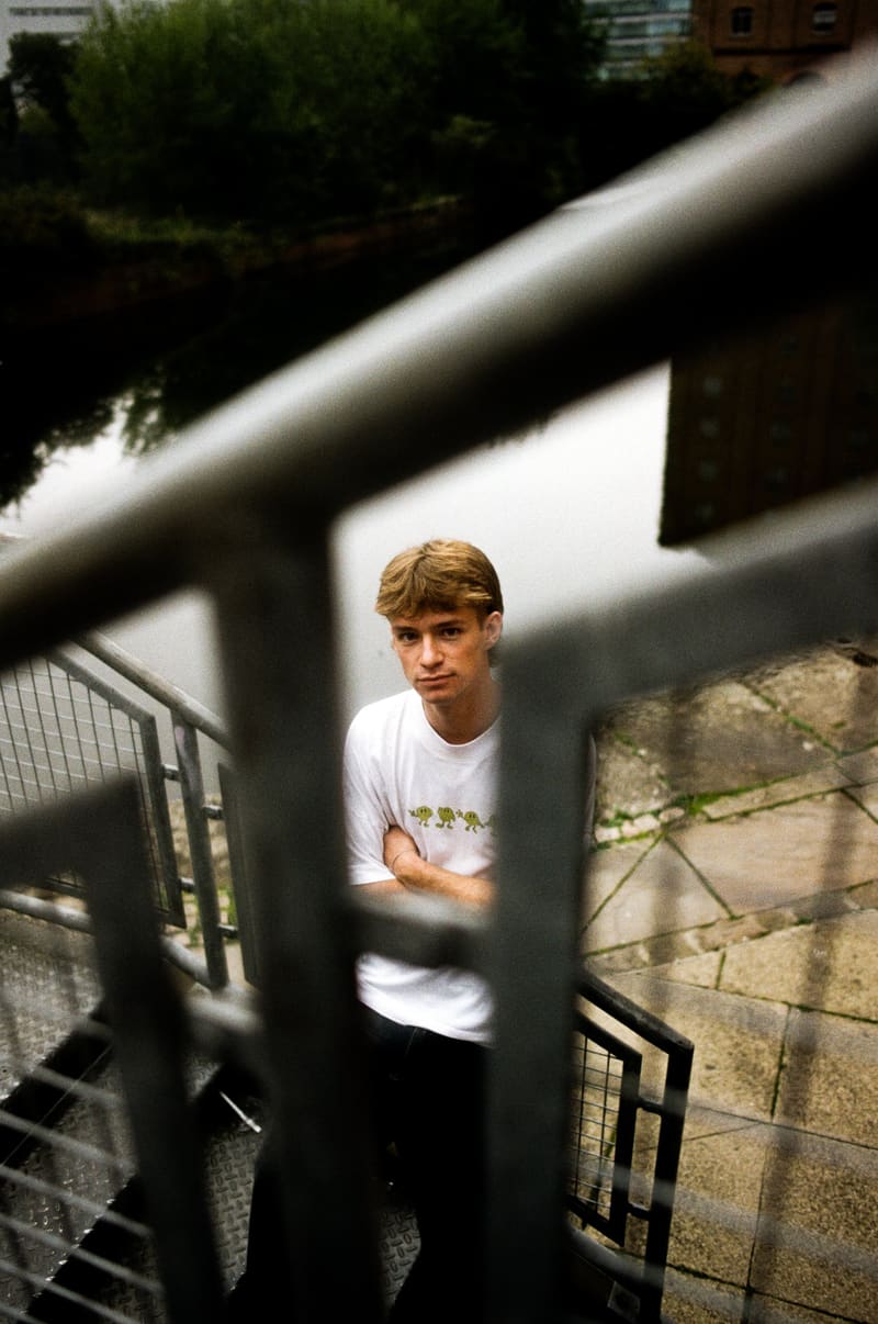Cam Smith in a white T-shirt, framed through the bars of a stair railing beside a canal